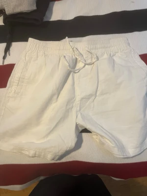 Vita linneshorts med snörning lagee 157 - Säljer ett par vita shorts i linne med elastisk midja och snörning framtill. Shortsen har sidofickor och en bakficka, perfekt för sommardagar. De har en avslappnad passform och är riktigt sköna att bära.
