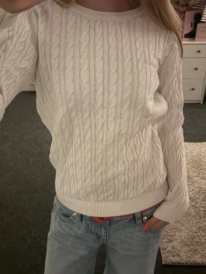 Vit kabelstickad tröja - Säljer en klassisk vit kabelstickad tröja med rund hals och långa ärmar. Tröjan är gjord i ett mjukt material som känns skönt mot huden. Perfekt att styla med jeans för en clean look.🤍