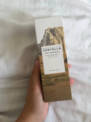 SKIN1004 Centella Cleansing Oil - Madagascar Centella Light Cleansing Oil från SKIN1004. Rengöringsolja med centella-extrakt, 200 ml. Kommer i en vit och beige kartong med naturmotiv och stilren design.
