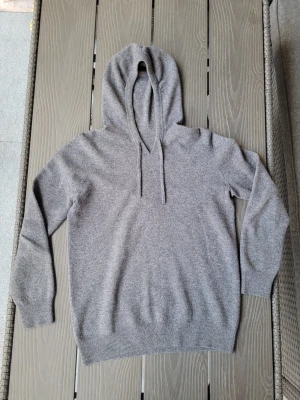 Grå stickad hoodie - Mysig grå stickad hoodie. Tillverkad i ett mjukt, stickat material som känns skönt mot huden. Klassisk passform med ribbade muddar vid ärmslut och nederkant. Perfekt för chill dagar eller när du vill ha en enkel och stilren look.
