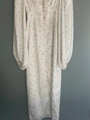 Vit långklänning från adoore i strl xs - Våt långklänning med små blåa blommor. Klänningen har en v-ringning, puffärmar och slits nedtill. Nypris är 1695kr, säljer för att den inte har kommit till användning. Pris går att diskutera💕