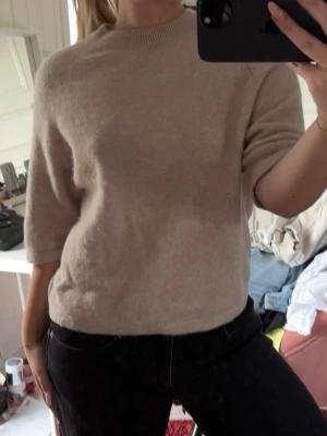 Beige stickad tröja med halvlånga ärmar - Beige stickad tröja med halvlånga ärmar och rund halsringning.