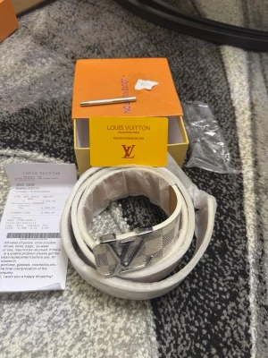 Vit LV bälte - Snyggt bälte från LV i vitt och beige med klassiskt rutigt mönster och silverfärgat LV-spänne. Bältet har exklusiv känsla och levereras med originalask och kvitto. Perfekt accessoar för att lyfta din outfit.