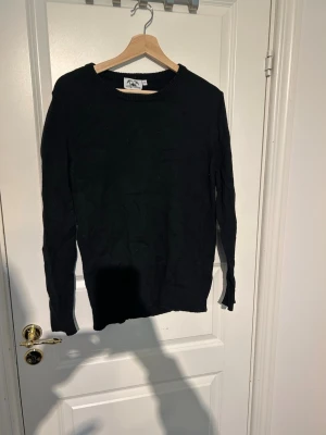 Svart stickad tröja från Stilgruvan - En klassisk svart stickad tröja från Stilgruvan i storlek M. Tröjan har rund halsringning och ribbade muddar vid ärmslut och nederkant. Perfekt för lager på lager och enkel att matcha med olika outfits.