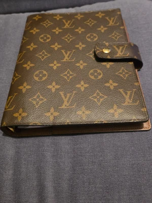 Louis Vuitton Large Agenda - Large agenda från Louis Vuitton i klassiskt monogrammönster med guldknapp. Perfekt för dig som gillar lyxiga accessoarer och vill ha något som sticker ut.  Mått: 18.5 x 23 x 3 cm