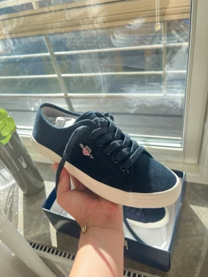 Helt nya GANT-skor - Säljer ett par helt nya GANT sneakers i mörkblått med vita detaljer. Aldrig använda ända som saknas är orginalkartong men kommer i en helt ny skokartong. Stilrena och passar till allt!🥰 Storlek: 36 Skick: helt nya från kartong
