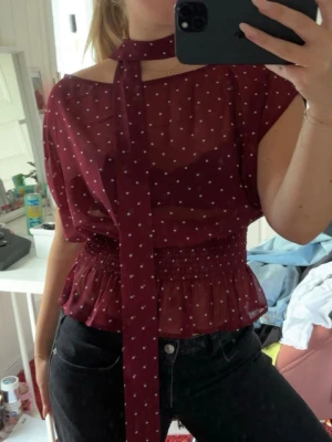 Vinröd prickig blus med scarfdetalj - Snygg vinröd blus med vita prickar och transparent material. Använd ett fåtal gånger.