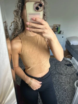 Beige croppad ärmlös linnetopp - Snygg beige croppad linnetopp med rund halsringning och figurnära passform. Toppen är ärmlös och har en enkel, stilren design som passar perfekt till både jeans och kjol. Materialet känns mjukt och bekvämt mot huden.