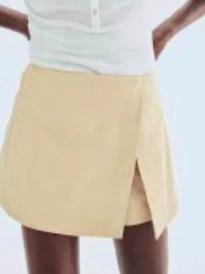 Beige omlott skort - Trendig beige skort med omlottdesign och kort passform. Tillverkad i ett lätt och mjukt tyg som ger en stilren look. Perfekt för dig som vill ha en mix mellan kjol och shorts. Enkel att matcha med olika toppar. Aldrig använd- nypris 350kr