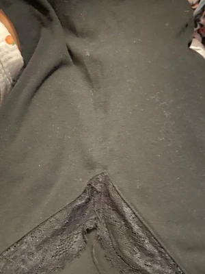 Svart blus med spetsdetalj - Snygg svart blus med V-formad spetsdetalj framtill. Tillverkad i mjukt tyg med dekorativ spets som ger en trendig look. Perfekt att matcha med jeans eller kjol för en cool outfit.