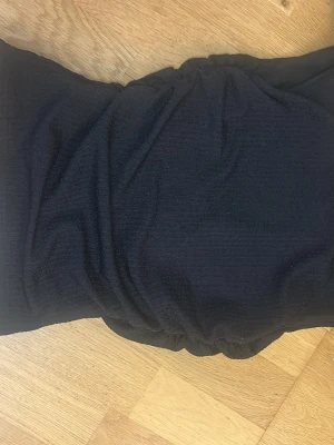 Svart baddräkt med knytband - Säljer en svart baddräkt med trendigt knytband på ena axeln. Materialet är ribbat och stretchigt vilket ger en snygg och bekväm passform. Perfekt för strand eller poolhäng i sommar!