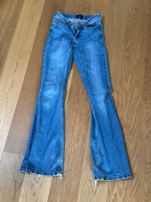 Blå bootcut jeans från Vero Moda - Snygga blå bootcut jeans från Vero Moda med slitna detaljer och råa kanter vid bensluten. Jeansen har klassisk femficksmodell, normalhög midja och är tillverkade i denim med lätt stretch. Perfekta för en avslappnad och trendig look.