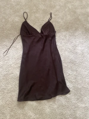 Brun satin slipklänning från bikbok - Snygg brun kort slipklänning i satin med tunna axelband och v-ringad urringning. Klänningen har en enkel och elegant design som ger en mjuk och följsam känsla. Perfekt för dig som gillar minimalistisk stil.