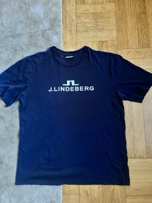Marinblå J.Lindeberg t-shirt - Snygg marinblå t-shirt från J.Lindeberg i storlek S med klassisk logga tryckt i vitt på bröstet.                                                             Fraktar inom 24h🚚💨