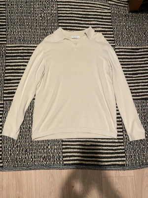 Beige stickad tröja med krage - En stilren beige stickad tröja med lång ärm och klassisk krage. Tröjan har en rak passform och är tillverkad i ett mjukt, tunt stickat material. Perfekt för lager-på-lager och enkel att matcha med olika outfits.