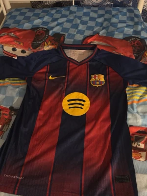 Barcelona matchtröja Nike röd/blå - Säljer en FC Barcelona matchtröja från Nike i klassiska rödblå ränder. Tröjan har klubbmärke och Nike-logga på bröstet, samt Spotify och UNHCR-loggor. Tillverkad i lätt och ventilerande Dri-FIT-material, perfekt för fotboll eller träning.