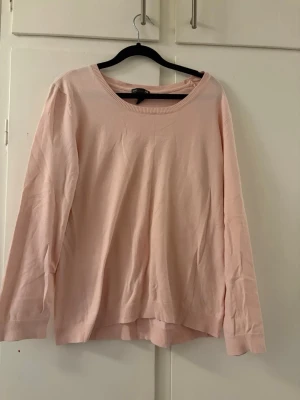 Ljusrosa basic tröja med rund hals - En enkel och mjuk ljusrosa tröja med rund halsringning och långa ärmar. Tröjan har en avslappnad passform och ribbade muddar vid ärmslut och nederkant. Perfekt att matcha med jeans eller kjol för en clean look.