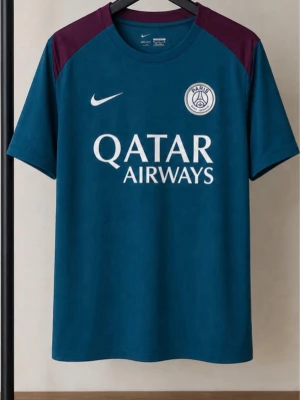 Blå PSG slimfit fotbollströja - Snygg blå slimfit fotbollströja med PSG-logga på bröstet och vita tryck. Tröjan har vinröda axelpartier och rund hals. Perfekt för träning eller match och har sponsortryck från Qatar Airways och Visit Rwanda.