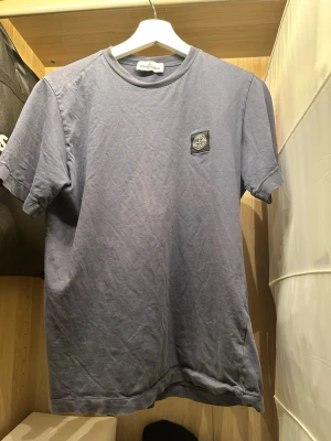 Blå t-shirt från Stone Island - Säljer en blå t-shirt från Stone Island med klassisk rund hals och korta ärmar. T-shirten har en patch med Stone Island-loggan på bröstet och är tillverkad i mjuk bomull. Perfekt för en avslappnad och stilren look.