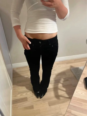 Svarta bootcut jeans med låg midja - Säljer ett par svarta jeans med låg midja och bootcut passform. Jeansen har klassiska fem fickor och stängs med knapp och dragkedja. Perfekta för dig som gillar en tidlös och stilren look.