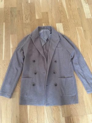 Beige dubbelknäppt stickad kavaj John Henric nypris 1999 - Storlek xs sitter som S, Snygg beige dubbelknäppt kavaj från John Henric med två stora framfickor och en bröstficka. Kavajen har en mjuk struktur, breda slag och är helfodrad med slät insida. Perfekt för en stilren och modern look. Aldrig använd har bara hängt i garderoben.