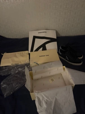Svarta Axel Arigato sneakers med fågel - Snygga svarta sneakers från Axel Arigato med vit sula och broderad fågel på sidan. Skorna har svarta skosnören, detaljer i mocka vid tån och grå häl. Perfekta för dig som gillar stilrena och trendiga sneakers.