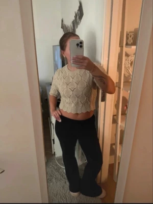 Beige stickad crop top från ONLY - Trendig beige stickad crop top från ONLY med korta ärmar och snyggt strukturmönster. Tröjan har vågig kant nertill och är perfekt för dig som gillar en modern och avslappnad stil. Materialet är mjukt och bekvämt, passar till många olika outfits.