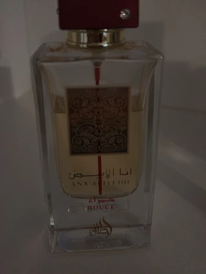Ana Abiyedh Rouge parfym - Ana Abiyedh Rouge parfym i en rektangulär glasflaska med guldfärgad detalj och röd linje på framsidan. Flaskan har en röd kork med en liten sten och arabiska samt engelska texter på etiketten. Doften är elegant och flaskan känns lyxig.