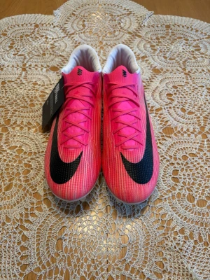 Nike fotbollsskor  - Säljer ett par snygga fotbollsskor från Nike i en stark rosa färg med stor svart swoosh på ovansidan. Skorna har snörning, låg profil och vit insida. Perfekta för dig som vill sticka ut på planen och ha bra grepp på gräs.