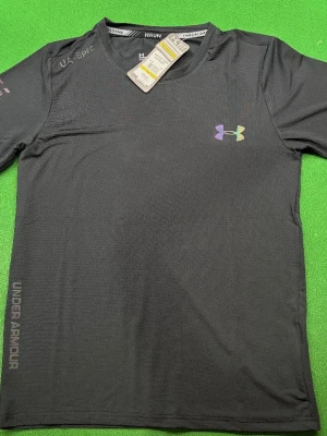 Svart träningsset från Under Armour - Snyggt svart träningsset från Under Armour med t-shirt och shorts. Båda plaggen har diskreta loggor i regnbågsfärg och är tillverkade i ett lätt, snabbtorkande funktionsmaterial. Perfekt för löpning eller gym. Elastisk midja på shortsen och rund hals på t-shirten. Fråga om mer bilder.