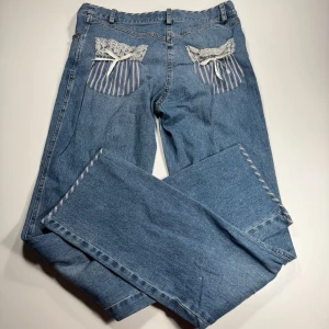 Luisa Spagnoli Blå jeans med spets och randiga detaljer - Unika blå jeans med raka ben och dekorativa spets- och randiga detaljer på bakfickorna samt vid ficköppningarna fram. 0402