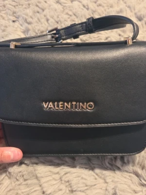 Svart handväska från Valentino - Inte mkt använd. Fin. Det enda jag kan se är det på undersidan av väskan, syns på bild. Inget som stör.