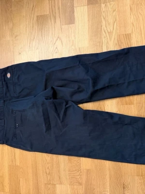 Svarta Dickies 874 Original Fit chinos - Klassiska svarta Dickies 874 Original Fit chinos med rak passform. Byxorna har två bakfickor, blixtlås i gylfen och tydlig Dickies-logga ovanför ena bakfickan. Materialet är slitstarkt och passar perfekt till en streetwear-look. W32 L30
