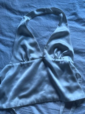 Vit halterneck topp i satin från Zara - Säljer en snygg vit halterneck topp från Zara i glansigt satinmaterial. Toppen har djup v-ringning och knytning i ryggen , perfekt för att skapa en trendig look. Passar till både jeans och kjol för en cool stil. Den har lite sminkfläckar som borde kunna gå bort i tvätten men annars tänker man inte på det så mycket