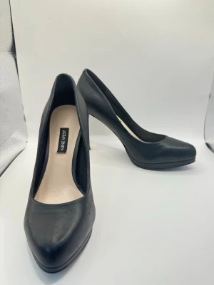 Svarta pumps från Nine West strl 38 äkta läder - Stilrena svarta pumps från Nine West med spetsig tå och hög klack. Skorna är tillverkade i slätt material och har en klassisk siluett som passar till många olika looks. Perfekta för dig som vill ha en tidlös och elegant sko.