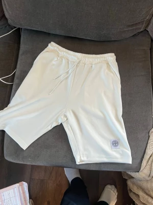 Vita shorts från Stone Island - Säljer ett par vita shorts från Stone Island med elastisk midja och snörning. Shortsen har en clean look och en patch med Stone Island-loggan på benet. Perfekta för sommaren och riktigt sköna att bära till vardags. Är storlek S men passar M/L
