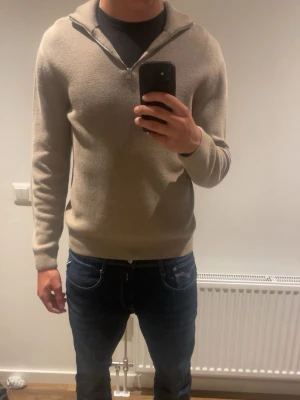 Jack&Jones Beige halvzip tröja i ullmix  - Snygg beige tröja med halv dragkedja och hög krage. Tillverkad i mjuk ullmix som känns skön mot huden. Långärmad modell med ribbade muddar vid ärmslut och nederkant. Perfekt för stilren look. 