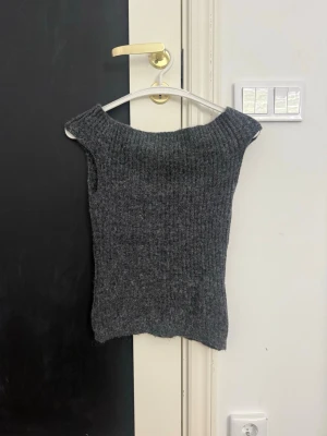 Mörkgrå stickad off shoulder topp - Säljer en ribbstickad mörkgrå ärmlös off shoulder topp. Materialet ser ut att vara mjukt och lite fluffigt, troligen ullblandning. Perfekt att styla över en skjorta eller t-shirt för en trendig lager-på-lager-look.