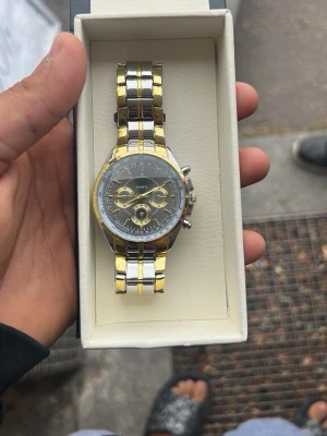 Guld- och silverfärgad kronografklocka - Snygg klocka med både guld- och silverfärgad länkarmband och svart urtavla. Klockan har flera små urtavlor och detaljerade visare. Perfekt accessoar för dig som vill sticka ut lite extra.