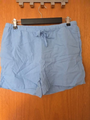 Ljusblåa shorts med snörning - Snygga ljusblå shorts med avslappnad passform och snörning i midjan. Perfekta för varma dagar och enkla att matcha med olika toppar. Tillverkade i ett lätt och bekvämt material som känns svalt mot huden.