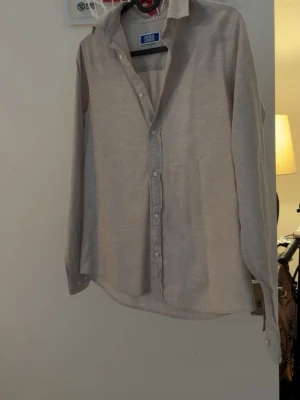 Beige skjorta från Jack & Jones - Klassisk beige skjorta från Jack & Jones med lång ärm och knappar framtill. Skjortan har en avslappnad passform och är tillverkad i mjukt bomullsmaterial. Perfekt till jeans eller chinos för en clean look.