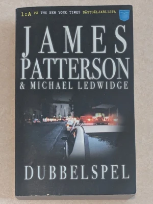 Dubbelspelet av James Patterson - Spännande roman av James Patterson och Michael Ledwidge. Boken har ett svart omslag med polisbil och utryckningsljus i stadsmiljö. Perfekt för dig som gillar thrillers och snabba vändningar. Utgiven av Pocketförlaget, svensk text.