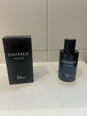 Dior Sauvage Eau de Parfum - Dior Sauvage Eau de Parfum med elegant mörkblå glasflaska och matchande svart kartong. Flaskan har en stilren, rund form och tydlig logga framtill. En ikonisk doft som utstrålar lyx och modernitet.