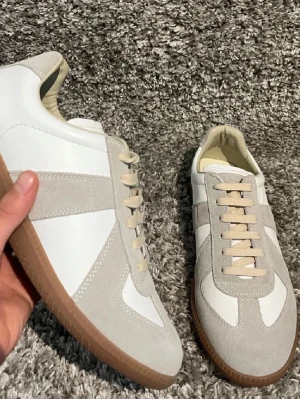 Vita och beige sneakers med gummisula - Stilrena sneakers i vitt och beige med klassisk design. Ovandelen är i en mix av mocka och slätt material, och skorna har beige snören samt en snygg ljusbrun gummisula. Perfekta för en clean och avslappnad look.