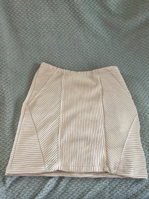 Beige ribbad kortkjol - Säljer en beige kortkjol med ribbad struktur och snygga paneler framtill. Kjolen har en enkel, stilren design och är lätt att matcha med olika toppar. Perfekt för dig som gillar en clean och modern look.