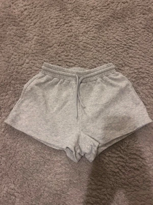 Grå mjukisshorts från H&M - Ett par ljusgrå mjukisshorts från H&M med resår i midjan. Tillverkade i mjukt sweatshirtmaterial som är perfekt för chill dagar eller träning. Klassisk och enkel design utan fickor eller tryck.