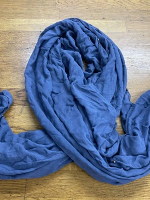 Grå sjal med små pärldetaljer - En stor, mjuk sjal i grå tyg med små pärldetaljer längs kanten. Sjalen har en lätt skrynklig struktur och är perfekt att svepa runt halsen för en avslappnad look. Materialet känns tunt och luftigt, vilket gör den enkel att styla på olika sätt.