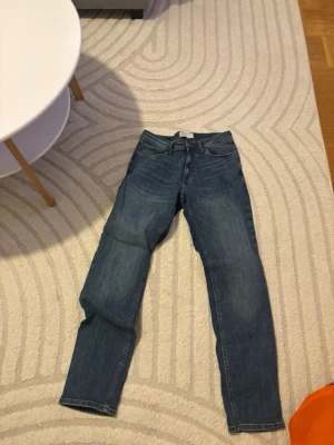 Blå slim fit jeans från denim co. - Säljer ett par blå slim fit jeans från denim co. i storlek W30/L32. Klassisk femficksmodell med normalhög midja och raka ben. Jeansen har snygga slitningar och är tillverkade i ett mjukt denimtyg som sitter skönt hela dagen.