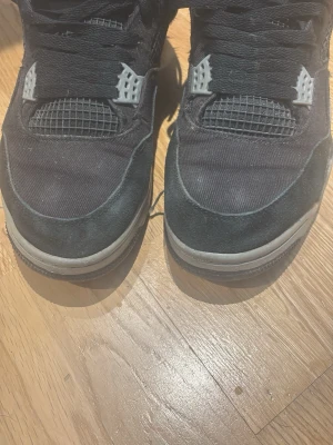 Svarta Air Jordan 4 sneakers - Säljer ett par svarta Air Jordan 4 sneakers med vita detaljer och klassisk Jumpman-logga på hälen. Skorna har meshpaneler, mockaliknande material och plastdetaljer vid snörningen. Perfekta för dig som gillar streetwear och ikoniska sneakers. storleken är 43 men passa även 42 Skorna har gått sönder!