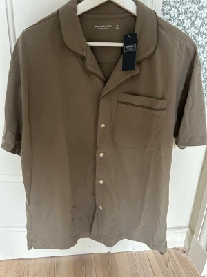 Pyjamasskjorta Abercrombie & Fitch - Snygg pyjamasskjorta från Abercrombie & Fitch med korta ärmar, klassisk krage och knappstängning framtill. Skjortan har en bröstficka och är gjord i mjukt material för extra komfort. Perfekt för chilliga kvällar hemma.